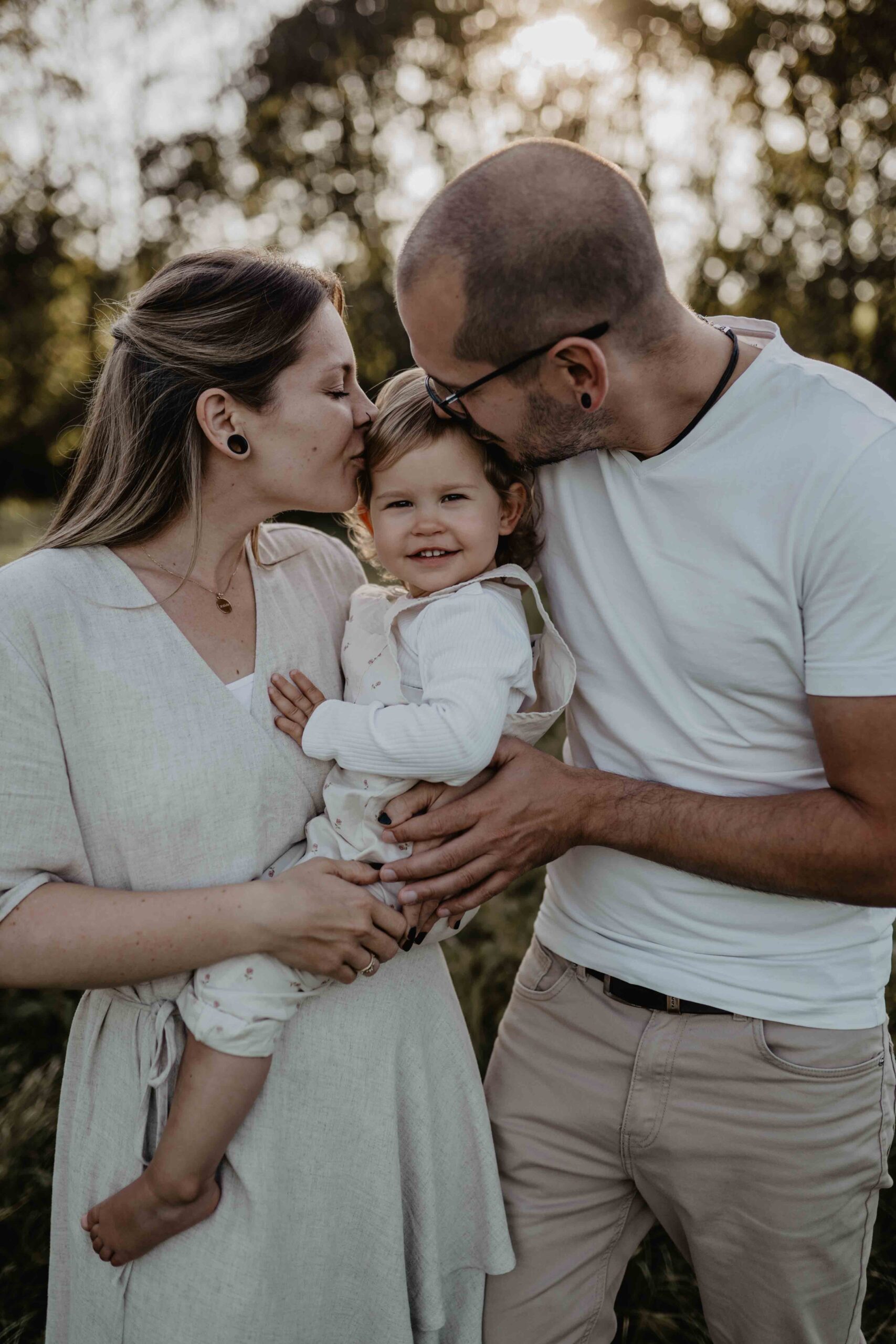 Familienfotos in Wien und Umgebung - Mama und Papa haben ihre Tochter am Arm und geben ihr ein Bussi