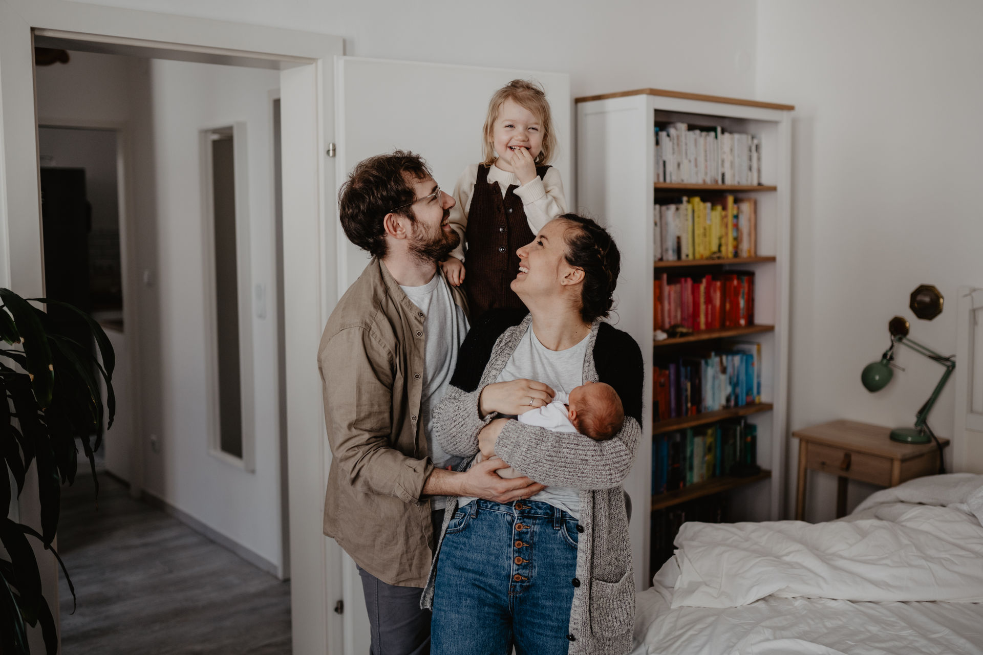 Babyfotos in Wien mit großer Schwester, das Mädchen lacht in die Kamera, während die Eltern das Mädchen anschauen