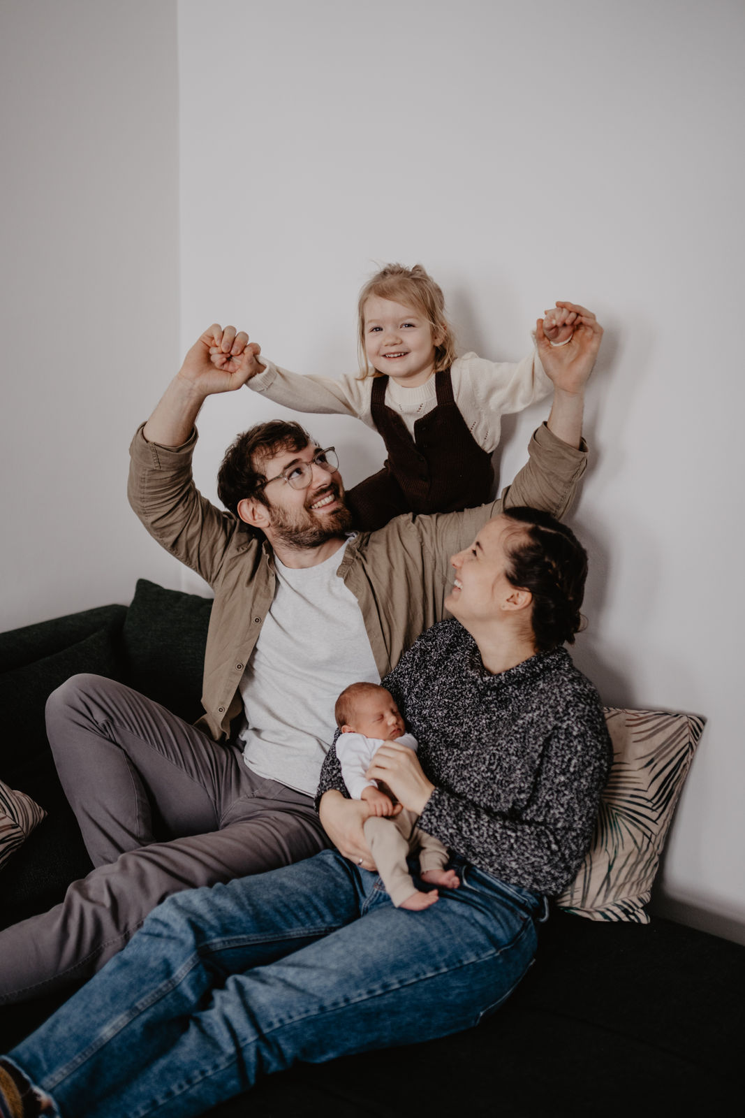 Eine Familie sitzt bei einem Babyfotoshooting gemeinsam auf der Couch, alle albern herum und lachen. Babyfotos Wien und Mödling